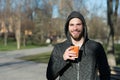Happy macho in hood hold disposable coffee cup in sunny park. Bearded man smile with takeaway drink on fresh air. Coffee or tea mo