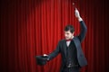 Happy magician or illusionist is showing magic trick with his wand. Red curtains in background Royalty Free Stock Photo