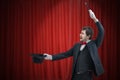 Happy magician or illusionist is showing magic trick. Red curtains in background Royalty Free Stock Photo