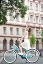 Happy maiden enjoys bike ride on the city streets against background of high-rise architectural building.