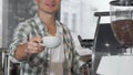 Happy male barista smiling holding out cup of tasty coffee to the camera Royalty Free Stock Photo