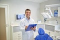 Happy male dentist with clipboard at dental clinic