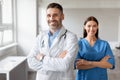 Happy male doctor and female nurse colleagues, wearing coats, standing with folded arms, posing at medical office Royalty Free Stock Photo