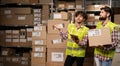 Happy male factory manager using digital tablet in warehouse while standing against goods boxes and worker with parcel Royalty Free Stock Photo