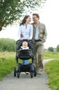 Happy male and female parents walking with their child in baby carriage Royalty Free Stock Photo