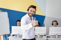 Happy male hotline operator smiling and showing thumb up gesture at modern open space office