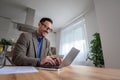 Happy male manager wearing elegant suit typing e-mail on laptop while working at home office