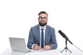 happy male newscaster sitting at table with laptop, notepad and microphone,