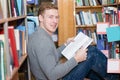 Happy male student with book sitting on floor in library Royalty Free Stock Photo