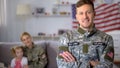 Happy male veteran of US army smiling at camera, wife and daughter on background