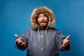 Happy male in winter jacket with fur on empty blue background Royalty Free Stock Photo
