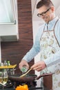 Happy man adding white wine to saucepan while cooking in kitchen