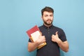 Happy man with a beard and books and notebooks in his hand shows a thumbs up and smiles, isolated on a blue background. Portrait Royalty Free Stock Photo