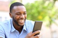 Happy man with black skin checking smart phone in a park Royalty Free Stock Photo