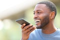 Happy man with black skin dictating text on cell phone