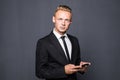 Happy business man in black suit typing sms on smartphone on grey Royalty Free Stock Photo