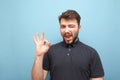 Happy man on a blue background smiles at the sign OK. Bearded man shows what he likes, looks at the camera, isolated on a yellow