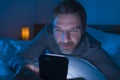 Happy man with blue eyes lying on bed late at night in dark light networking on mobile phone or online dating smiling relaxed Royalty Free Stock Photo