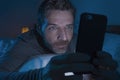 Happy man with blue eyes lying on bed late at night in dark light networking on mobile phone or online dating smiling relaxed Royalty Free Stock Photo