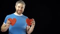 Happy man in blue tshirt holds two red heart shapes. Love, romance, dating, relationship concepts. Black background Royalty Free Stock Photo