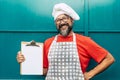 Happy man chef with white hat show empty paper menu for restaurant recipes or list - concept of people and work activity - Royalty Free Stock Photo