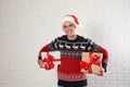 Happy man in Christmas sweater and Santa hat holding gift boxes near white brick Royalty Free Stock Photo