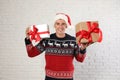 Happy man in  sweater and Santa hat holding gift boxes near white brick wall Royalty Free Stock Photo