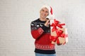 Happy man in Christmas sweater and  hat holding gift boxes near white brick wall Royalty Free Stock Photo