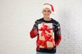 Happy man in Christmas sweater and Santa hat holding gift boxes near white brick Royalty Free Stock Photo