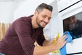 Happy man cleaning oven with rag and bottle spray Royalty Free Stock Photo