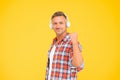 Happy man clench fist listening to music playing in modern earphones yellow background, audio