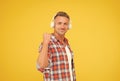 Happy man clench fist listening to music playing in modern earphones yellow background, audio