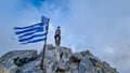 Happy man with climbing helmet on cloud covered mountain summit of Mytikas Mount Olympus, Greece. Greek flag on top Royalty Free Stock Photo