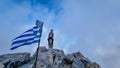 Happy man with climbing helmet on cloud covered mountain summit of Mytikas Mount Olympus, Greece. Greek flag on top Royalty Free Stock Photo