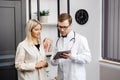 Happy man doctor showing tablet woman patient in clinic office interior. Health care, visit to family therapist, treatment of Royalty Free Stock Photo