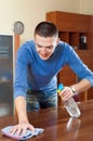 Happy man dusting table with rag and cleanser at home Royalty Free Stock Photo