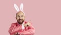 Happy man in Easter Bunny ears pointing finger at pink text copy space background