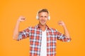 Happy man flex strong arms listening to music in modern headphones yellow background, sound power Royalty Free Stock Photo