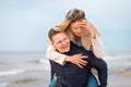 Happy man giving piggyback ride to his woman and laughing at beach. Smiling guy in love carrying on back her girlfriend Royalty Free Stock Photo