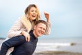 Happy man giving piggyback ride to his woman and laughing at beach. Smiling guy in love carrying on back her girlfriend Royalty Free Stock Photo