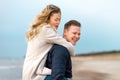 Happy man giving piggyback ride to his woman and laughing at beach. Smiling guy in love carrying on back her girlfriend Royalty Free Stock Photo