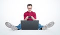 Happy man in glasses with joystick sitting on the floor in front of a laptop