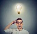 Happy man in glasses looking up at bright light idea bulb above head Royalty Free Stock Photo