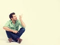 Happy man in green shirt and blue jeans sitting on the floor pointing at blank copy space Royalty Free Stock Photo