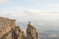 A happy man with his hands up high stands on top of a separately standing rock that is above the clouds against the Royalty Free Stock Photo