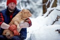 Happy man holding lovely dog in his hands in snowy forest. Smiling boy hugging adorable puppy in winter wood. Pet lover Royalty Free Stock Photo