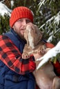 Happy man holding lovely dog in his hands in snowy forest. Smiling boy hugging adorable puppy in winter wood. Pet lover Royalty Free Stock Photo