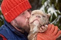 Happy man holding lovely dog in his hands in snowy forest. Smiling boy hugging adorable puppy in winter wood. Pet lover Royalty Free Stock Photo