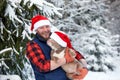 Happy man holding lovely dog in his hands wearing in a Santa hat in snowy forest. Smiling boy hugging adorable puppy in Royalty Free Stock Photo
