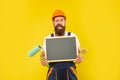 happy man housepainter in helmet and work clothes hold paint roller brush and blackboard